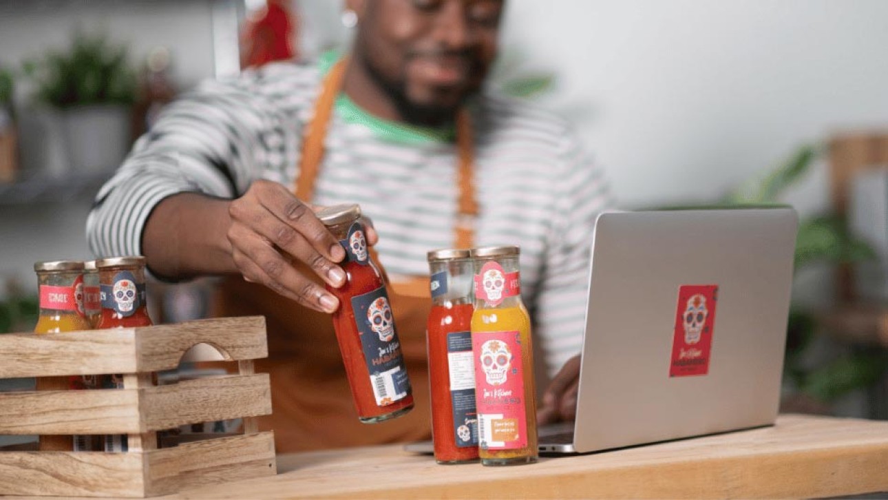 Man holding hot sauce bottle next to laptop