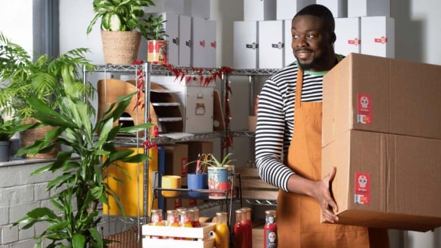 Man carrying two boxes hot sauce near shelf