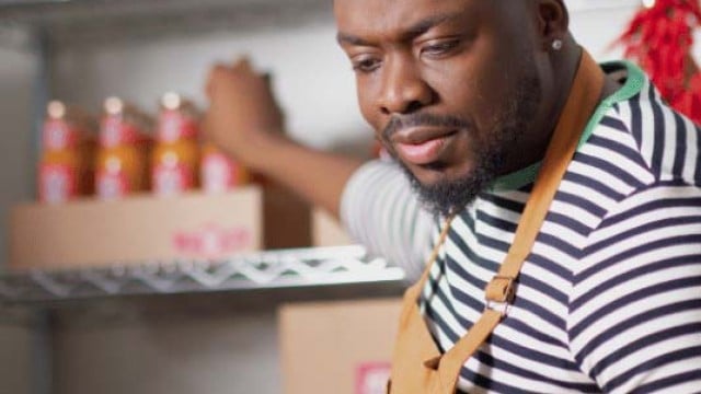 Man looking at laptop and holding hot sauce bottle