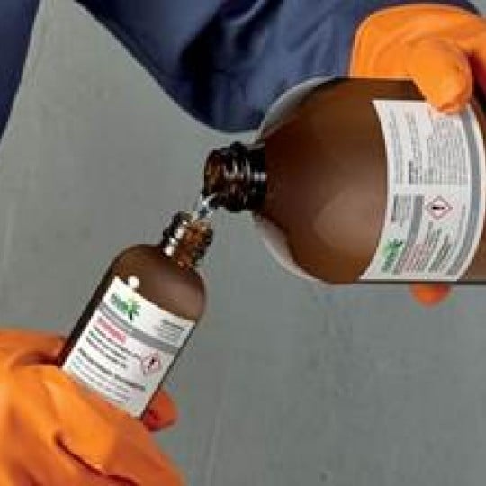 Persons hands pouring chemicals from one larger bottle into a smaller bottle with hazard labels on the bottles
