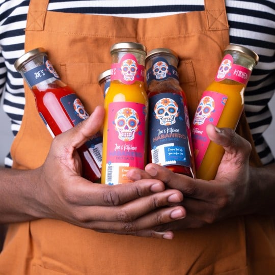 A man is holding several sauce bottles with different labels on them.