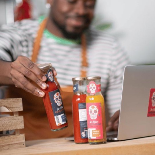 Man holding hot sauce bottle next to laptop
