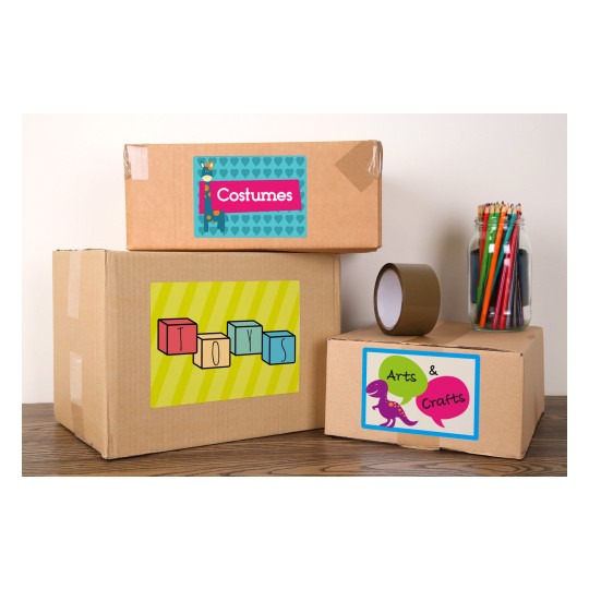 The image shows three labeled cardboard boxes stacked on a wooden surface. The boxes are labeled with 'Costumes,' 'Toys,' and 'Arts & Crafts,' featuring colorful designs. Next to the boxes, there's a jar filled with colored pencils and a roll of tape.