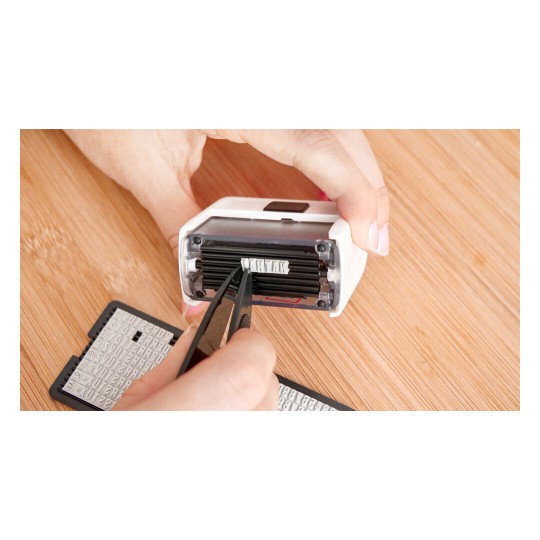 A person using tweezers to handle a piece of a label maker, showcasing the inner workings and letter blocks of the device.