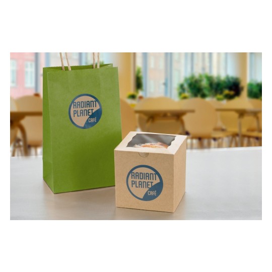 The image features a green paper bag and a brown cardboard box, both branded with 'Radiant Planet Café.' The bag has handles, while the box appears to contain a baked item. The background suggests a café setting with tables and plants.