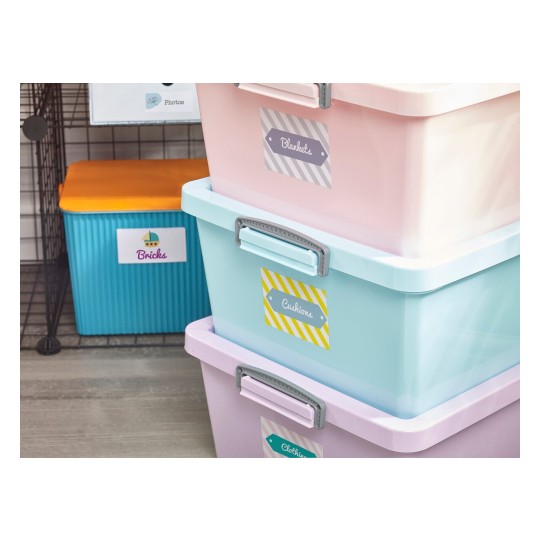 The image features several colorful storage bins stacked on top of each other. The bins are labeled with tags indicating their contents: blankets, cushions, and clothing. In the background, there’s a blue container labeled 'Bricks' and an orange box on top.