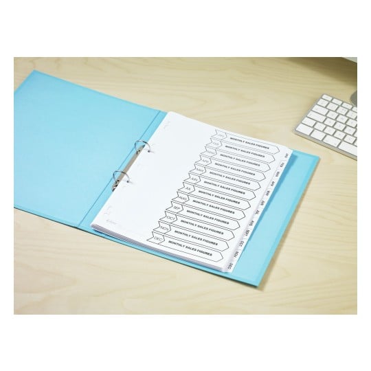 The image shows a binder filled with labeled tabs for each month of the year, indicating a focus on monthly sales figures. The binder is placed on a wooden desk next to a computer keyboard.