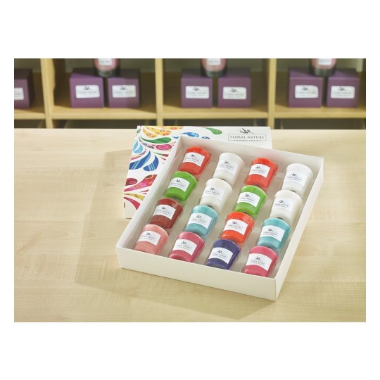The image features a neatly arranged box containing colorful candles of various shapes and sizes. Each candle has a label with the brand name 'Floral Nature.' The background showcases additional candles and decorative boxes.