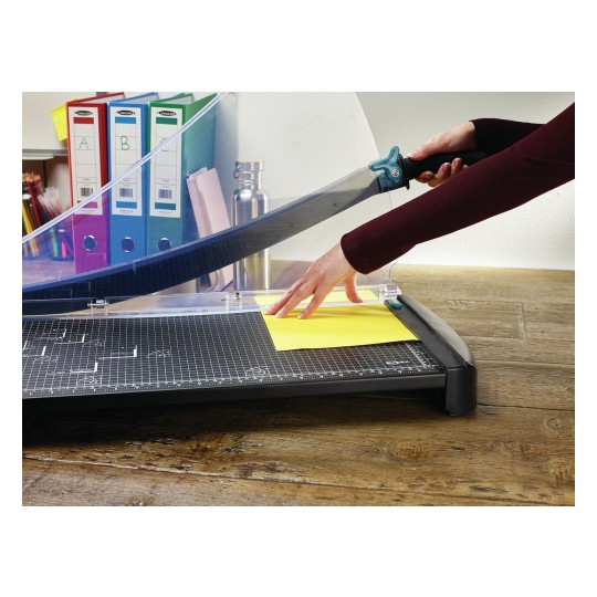 An image showing a person using a paper cutter to trim a yellow sheet of paper on a cutting mat. In the background, there are colorful binders and other office supplies.