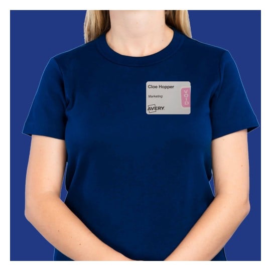 The image shows a person wearing a navy blue t-shirt with a name tag attached. The name tag displays 'Cloe Hopper' and the word 'Marketing,' along with a 'VOID' label. The background is solid blue.