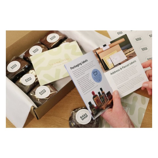 The image shows a box containing baked goods labeled 'Bake Shop', a thank you note, and an opened booklet discussing packaging and parcel labels.