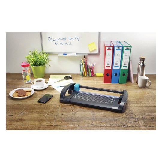 The image shows a workspace with a paper cutter, a cup of coffee, cookies on a plate, a water bottle, stationery, and colorful folders. There's also a smartphone and a list on the table, suggesting a creative or professional environment.