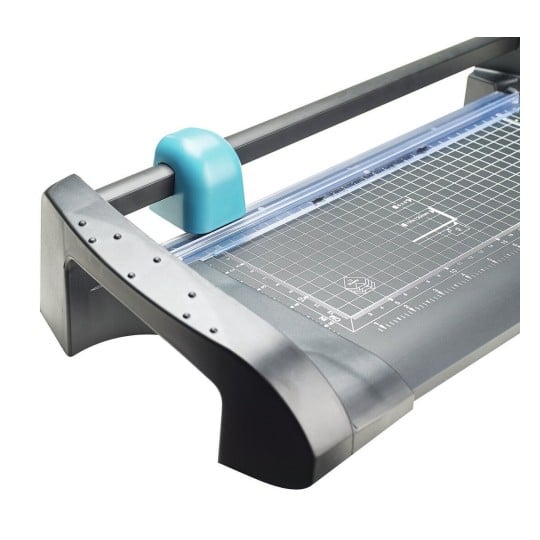 The image shows a cutting tool, specifically a guillotine paper cutter, featuring a clear cutting line guide and measurement grid on the surface.