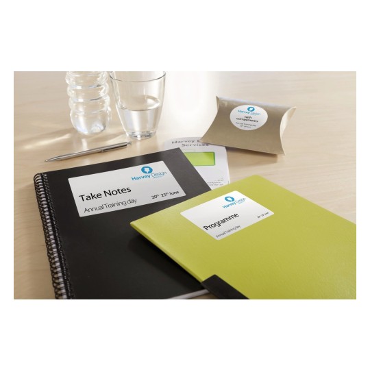 The image features a notepad labeled 'Take Notes', a green 'Programme' notebook, a pen, a glass of water, and a small package labeled 'with compliments', all arranged on a wooden surface, indicating a training event.