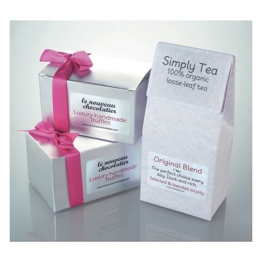 The image displays two silver gift boxes of luxury handmade truffles with pink ribbons. In addition, there is a packaging for organic loose-leaf tea labeled 'Simply Tea' and 'Original Blend'.