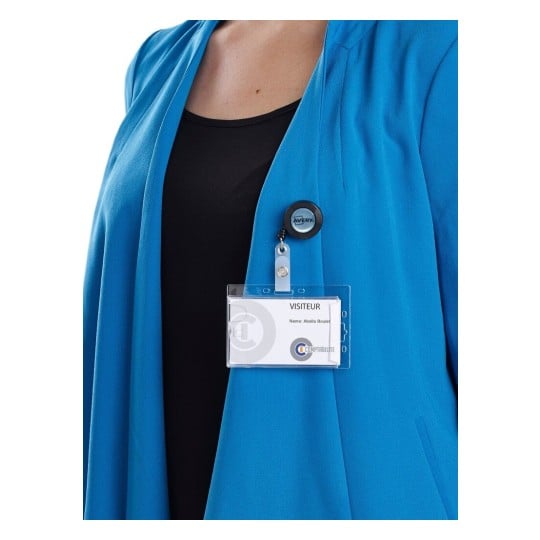The image shows a person wearing a blue blazer with a name badge visible. The badge indicates 'VISITEUR' and appears to contain a name and possibly an organization logo.