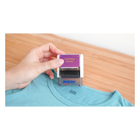 A person is using an Avery clothing stamp on a blue shirt. The stamp clearly reads 'Clothing Stamp'.