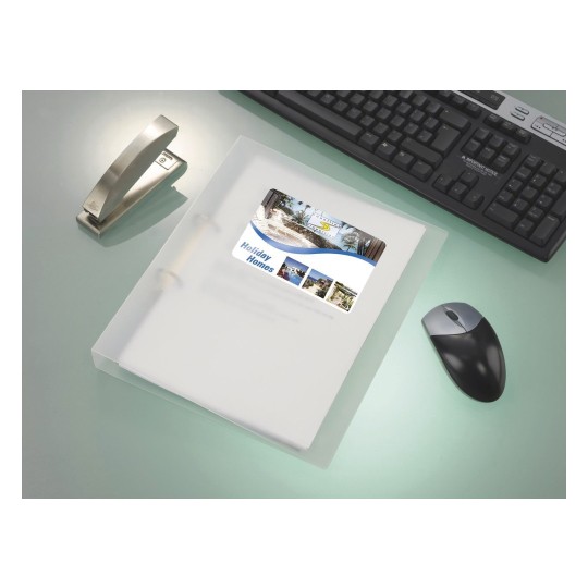 The image shows a workspace with a transparent folder containing a brochure for holiday homes, a stapler, a computer keyboard, and a mouse on a sleek surface.
