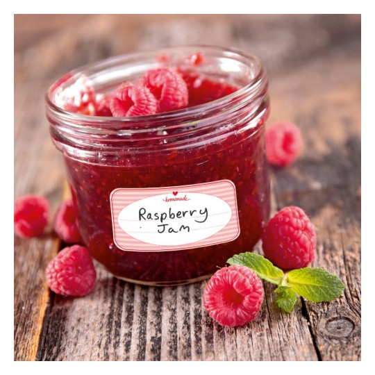 The image shows a jar of raspberry jam with fresh raspberries around it, resting on a wooden surface.