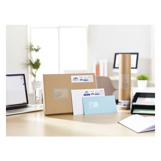 The image shows a workspace with a laptop, a large cardboard box, various letters, a cylindrical package, and an organized filing tray, all of which are labeled with addresses.