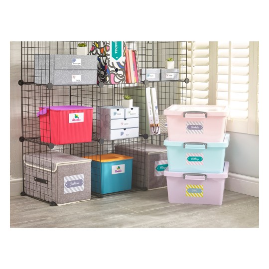 The image shows a storage shelf with various labeled containers in different colors. The shelf has baskets for organization, with items like puzzles, clothing, and other labeled categories. There are also small plants and decorative elements on the shelves, and the setting appears bright and organized.
