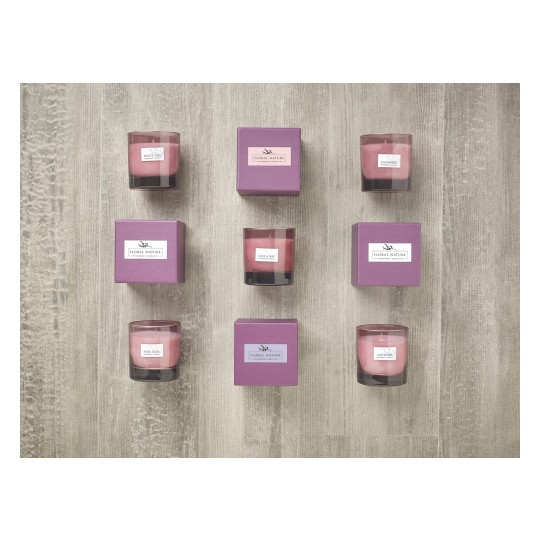 The image features decorative candles arranged on a wooden surface. There are four candles in glass holders labeled with scents such as 'White Lilac,' 'Lime & Basil,' 'Pink Rose,' and 'Lavender.' Each candle is paired with a matching purple packaging box, adding to the aesthetic appeal.