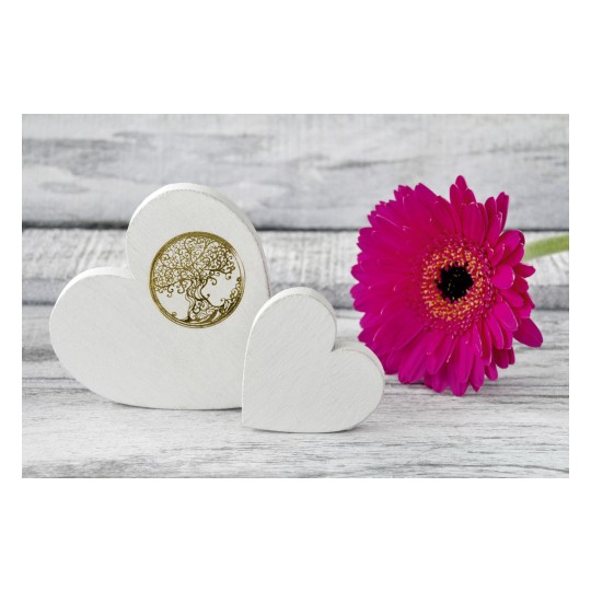 The image shows two white wooden hearts, one of which is decorated with a golden tree in a circle. Next to it, there is a pink flower on a wooden background.