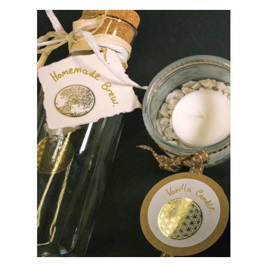 The image shows a glass bottle with a cork, marked with 'Homemade Brew' and a candle in a glass holder with white stones. The candle has a label with 'Vanilla Candle'.