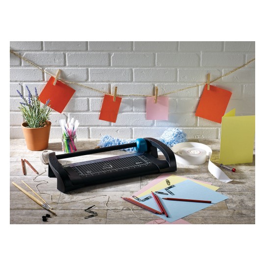 The image shows a creative workspace with a cutting machine, colored papers, pencils, washi tape, and a plant. Various colored cards are hanging on a string.