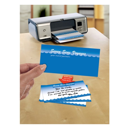 The image features a printer with travel-themed business cards being printed. The cards display the name 'Seven Seas Voyages' and a message addressed to 'Mrs. Clarke' with travel information. The design is colorful, featuring blue and white waves.