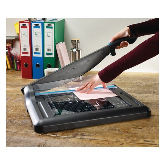 An image shows a person using a letter opener on a table. There are documents, a thermos, and colored binders in the background.
