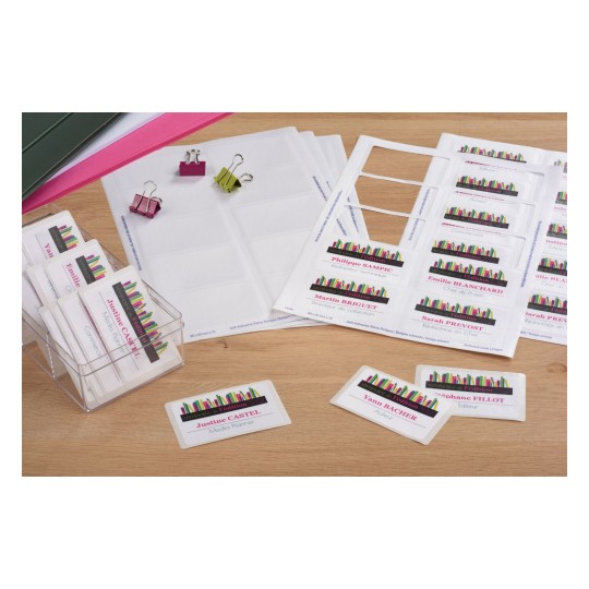 The image shows a collection of name badges and business cards arranged on a wooden surface. Various colored paper clips are present, along with sheets of adhesive name badge labels. The badges display names and roles related to a seminar or event, suggesting an organizational or professional context.