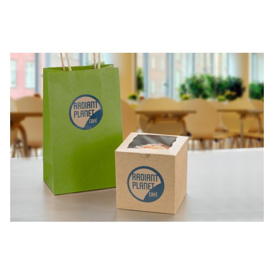 The image features a green paper bag and a brown cardboard box, both branded with 'Radiant Planet Café.' The bag has handles, while the box appears to contain a baked item. The background suggests a café setting with tables and plants.