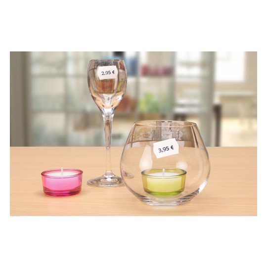The image features a table setting with three items: a wine glass with a price tag of 2,95 €, a pink candle in a glass holder, and a larger glass bowl with a green candle and a price tag of 3,95 €. The background is blurred, emphasizing the foreground items.