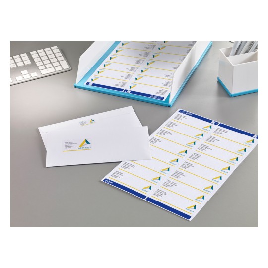 The image features a workspace with printed labels and envelopes. There is a sheet of labels with a design that includes a triangle logo and a blue border, along with an envelope displaying a name and address label. A keyboard and a pen holder are also visible.