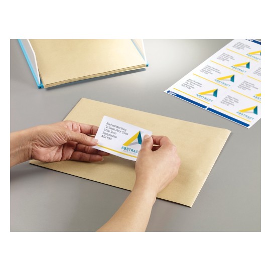 The image shows a hand placing a business card on a brown envelope. In the background, there are more cards and a folder.
