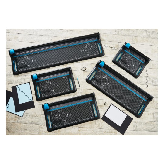 The image shows various sizes of paper cutters with blue-green handles, placed on a wooden floor. Next to the cutters are a few cards and a handful of paper clips.
