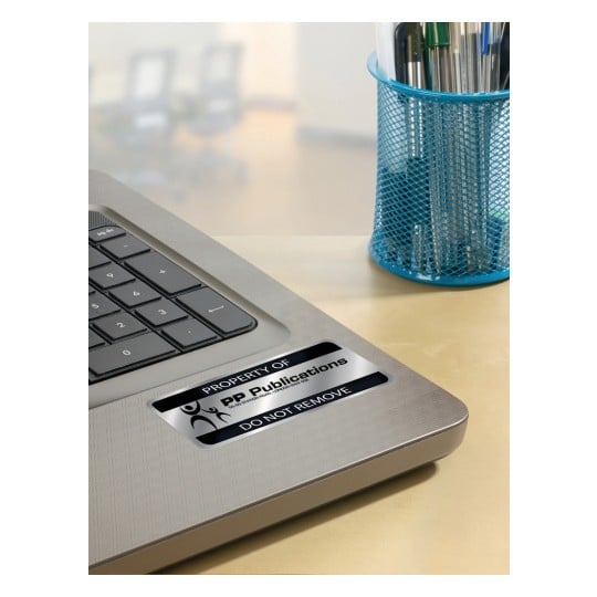 The image shows a laptop with a label indicating it is the property of PP Publications, alongside a blue pen holder filled with pens. The background appears to be an office environment.