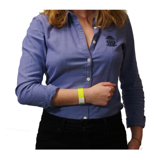 The image shows a woman wearing a blue shirt with a logo. She is holding her wrist, which has a yellow wristband on it.