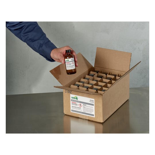 An individual holding a glass bottle with a label, while reaching into an open cardboard box filled with smaller containers arranged in rows.