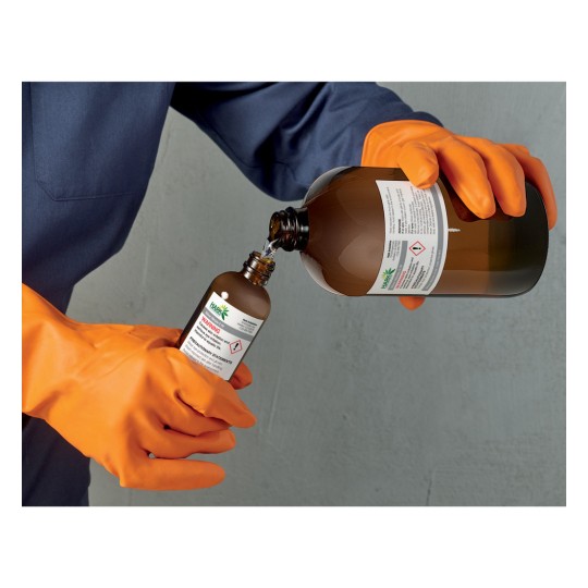 The image shows a person in orange gloves pouring a liquid from a large bottle into a smaller bottle, both labeled with warning signs. The person is wearing a blue long-sleeve shirt.