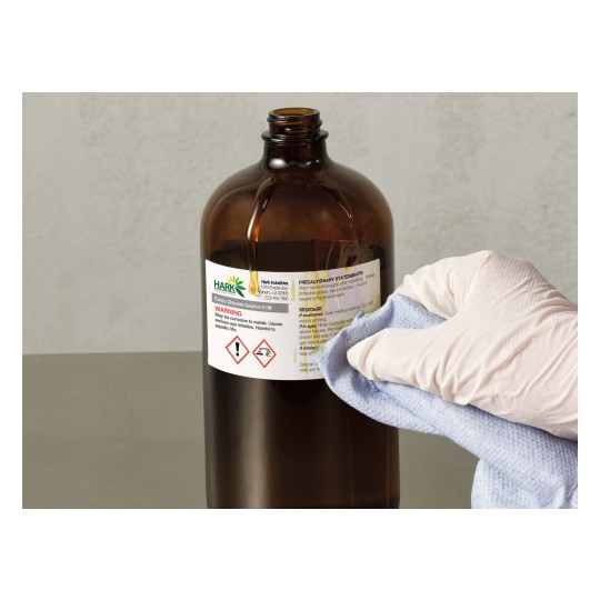 The image shows a brown glass bottle labeled with 'Ferric Chloride Solution 0.1M' and a warning about potential hazards. A hand wearing a glove is cleaning the bottle with a cloth.