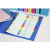 The image features an organized binder showing a monthly schedule with tabs for each month. The schedule lists various topics such as Business Summary, Market Trends, and Customer Issues. Surrounding the binder are colorful notebooks and binders.