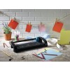 The image features a crafting workspace with a paper trimmer, colorful papers, clips, and stationery tools. There are red, pink, and yellow paper sheets displayed along a string, with a potted plant and various stationery items scattered on a wooden table.