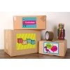 The image shows three labeled cardboard boxes stacked on a wooden surface. The boxes are labeled with 'Costumes,' 'Toys,' and 'Arts & Crafts,' featuring colorful designs. Next to the boxes, there's a jar filled with colored pencils and a roll of tape.