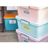 The image features several colorful storage bins stacked on top of each other. The bins are labeled with tags indicating their contents: blankets, cushions, and clothing. In the background, there’s a blue container labeled 'Bricks' and an orange box on top.