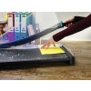 An image showing a person using a paper cutter to trim a yellow sheet of paper on a cutting mat. In the background, there are colorful binders and other office supplies.