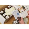 The image shows a box containing baked goods labeled 'Bake Shop', a thank you note, and an opened booklet discussing packaging and parcel labels.