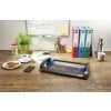 The image shows a workspace with a paper cutter, a cup of coffee, cookies on a plate, a water bottle, stationery, and colorful folders. There's also a smartphone and a list on the table, suggesting a creative or professional environment.