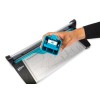 The image shows a person's hand holding a blue cutting device or trimmer, positioned above a cutting board with measurement markings. The cutting tool appears to have a specific compartment or feature and is likely used for trimming paper or materials.